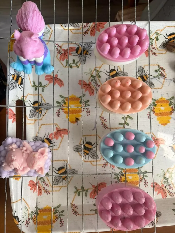 Four colorful massage bars alongside animal soaps on a bee print tablecloth.